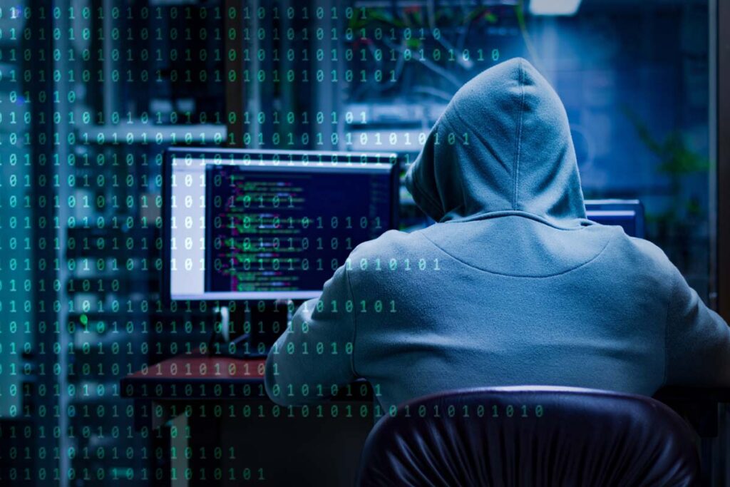 Back view of a hooded hacker using a computer, representing the EMSI data breach class action.
