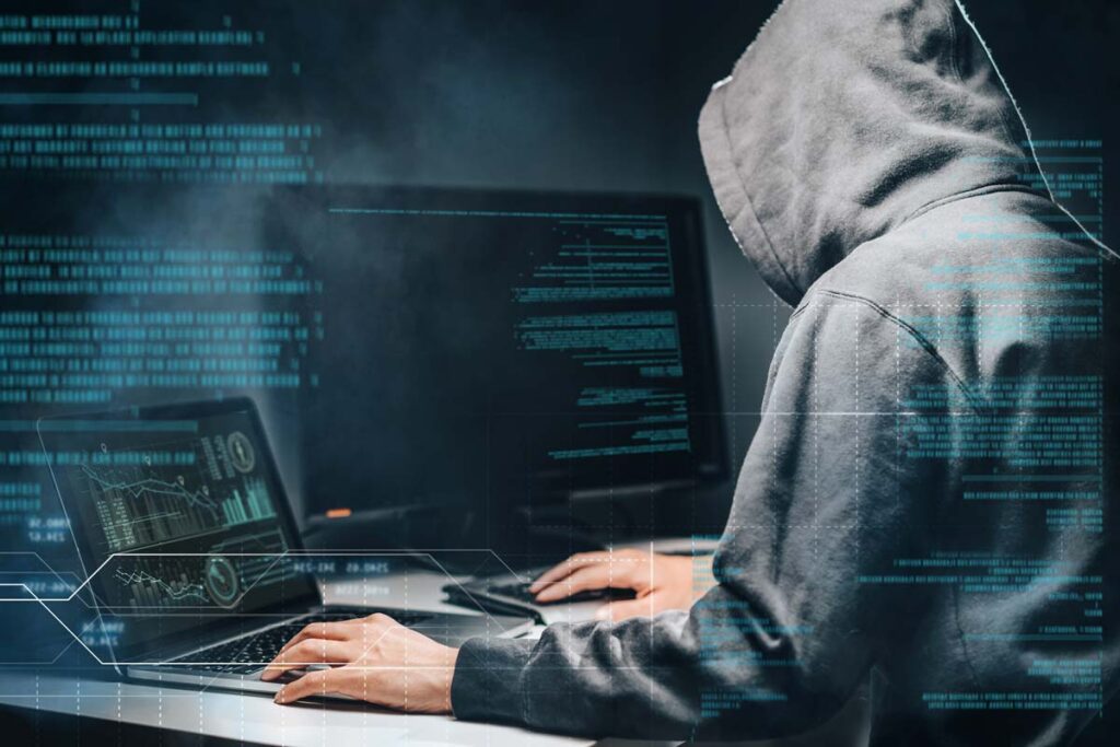 Closeup of a hooded hacker using a computer, representing the Webster Bank data breach class action lawsuit settlement.
