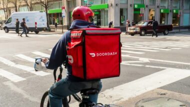 A Door Dash worker delivering on a bike with a Door Dash bag, representing the DoorDash class action.