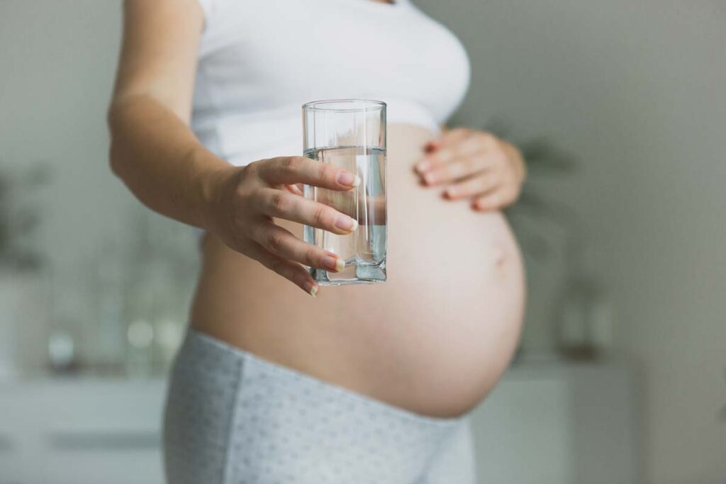 Close up of a pregnant woman drinking a glass of water, representing the fluoride trial.