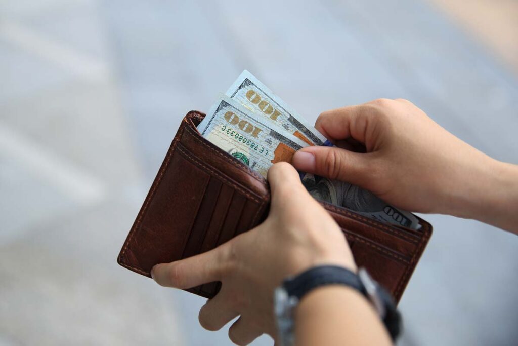 Close up of hands pulling cash from a wallet, representing recent class action rebates.