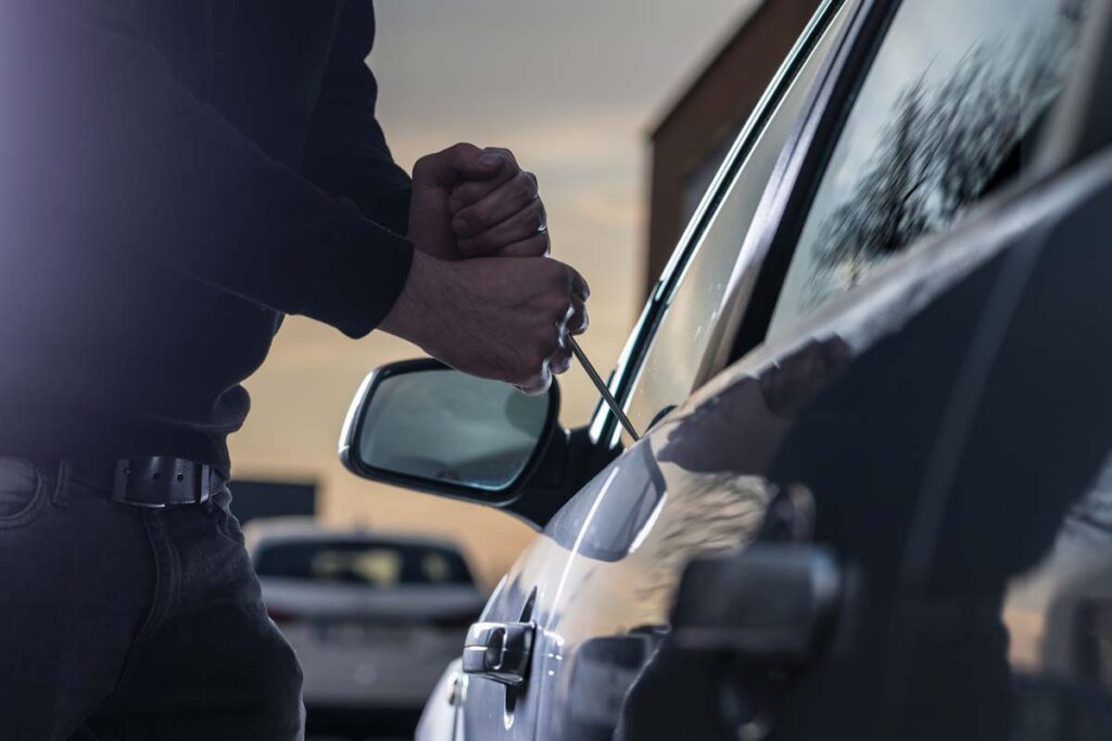 A thief using a tool to break into a car, representing the Kia theft class action lawsuit settlement.