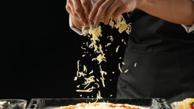 Cook putting shredded cheese on a pizza.