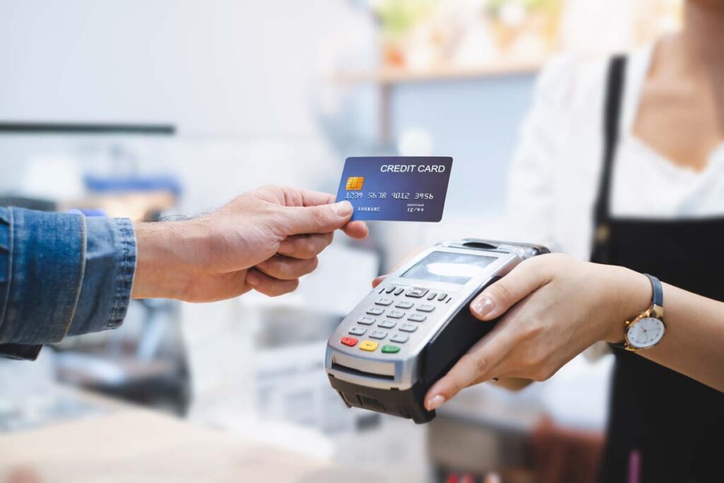 Close up of a man using a credit card on a POS machine, representing credit card late fees.