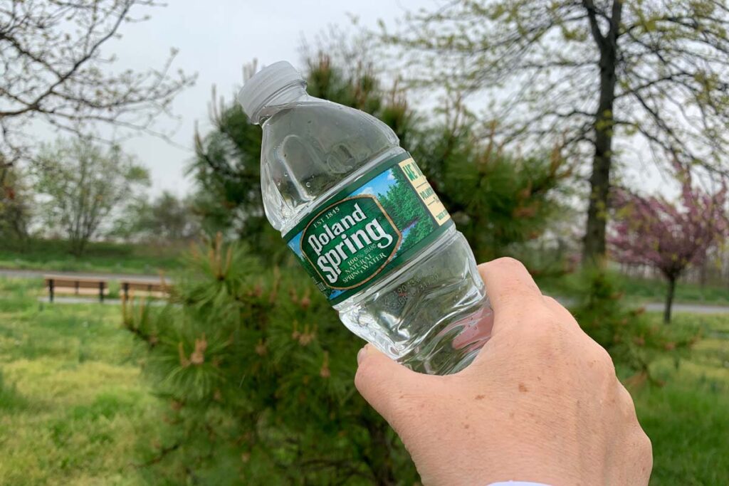 Close of a mans hand holding a Poland Springs water bottle, representing the Poland Springs class action.