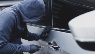 A hooded car thief using a screwdriver to break into a car, representing the Hyundai theft settlement.