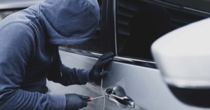A hooded car thief using a screwdriver to break into a car, representing the Hyundai theft settlement.