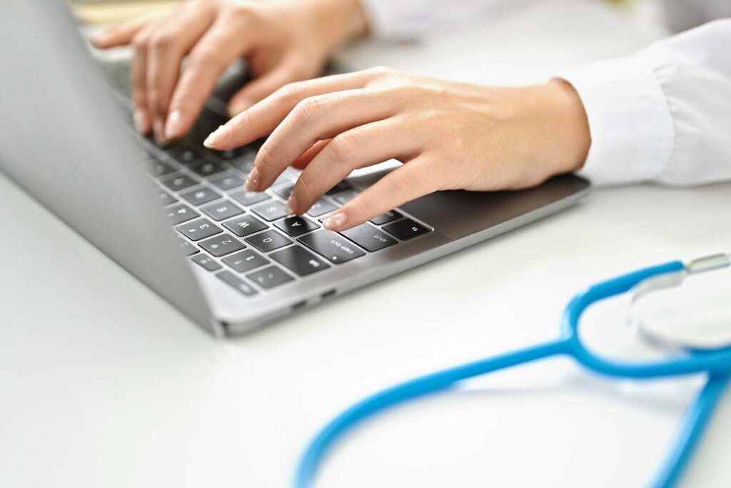 Close up of a female doctor typing on a laptop, representing the Avem Health Partners data breach settlement.
