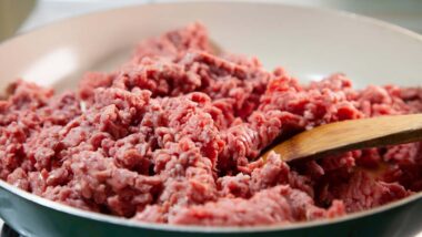 Close up of raw ground beef being cooked in a pan on a stove, representing the ground beef alert.