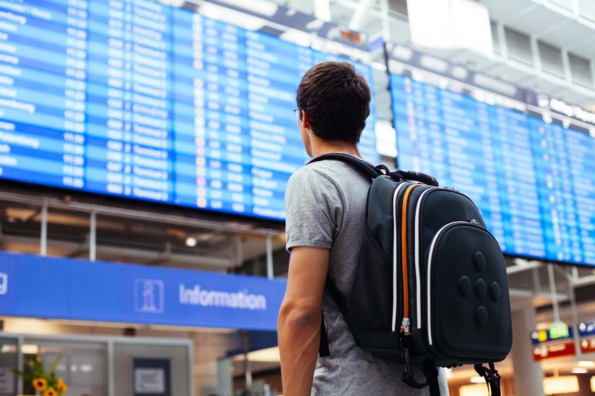 Back view of a man looking at a flight schedule board, representing airlines cash refunds.