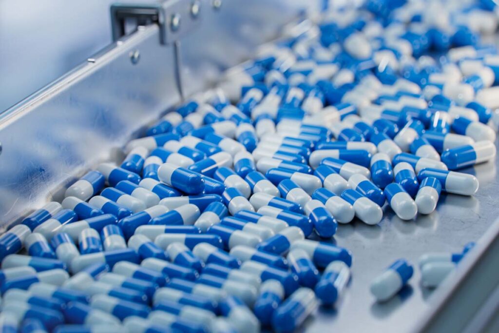 Close up of blue capsule pills on a conveyor belt, representing the pharmaceutical price-fixing lawsuit.
