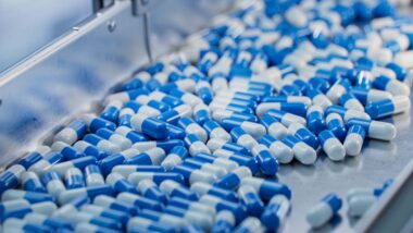 Close up of blue capsule pills on a conveyor belt, representing the pharmaceutical price-fixing lawsuit.