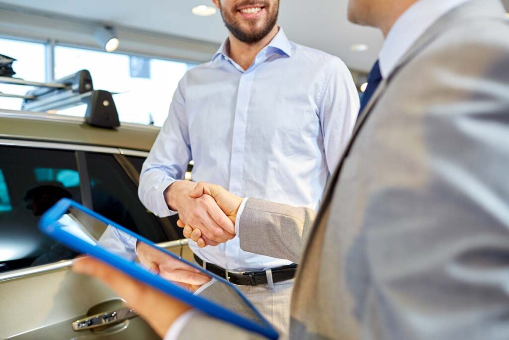 Close up of a car salesman holding a tablet and shaking hands with a customer, representing the Planet Nissan settlement.