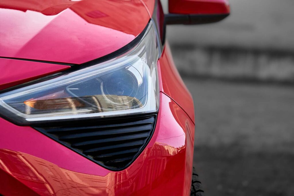 Close up of a headlight on a red car, representing April vehicle recalls.