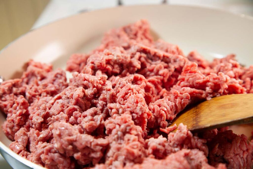 Close up of raw ground beef being cooked in a pan, representing the Walmart ground beef recall.