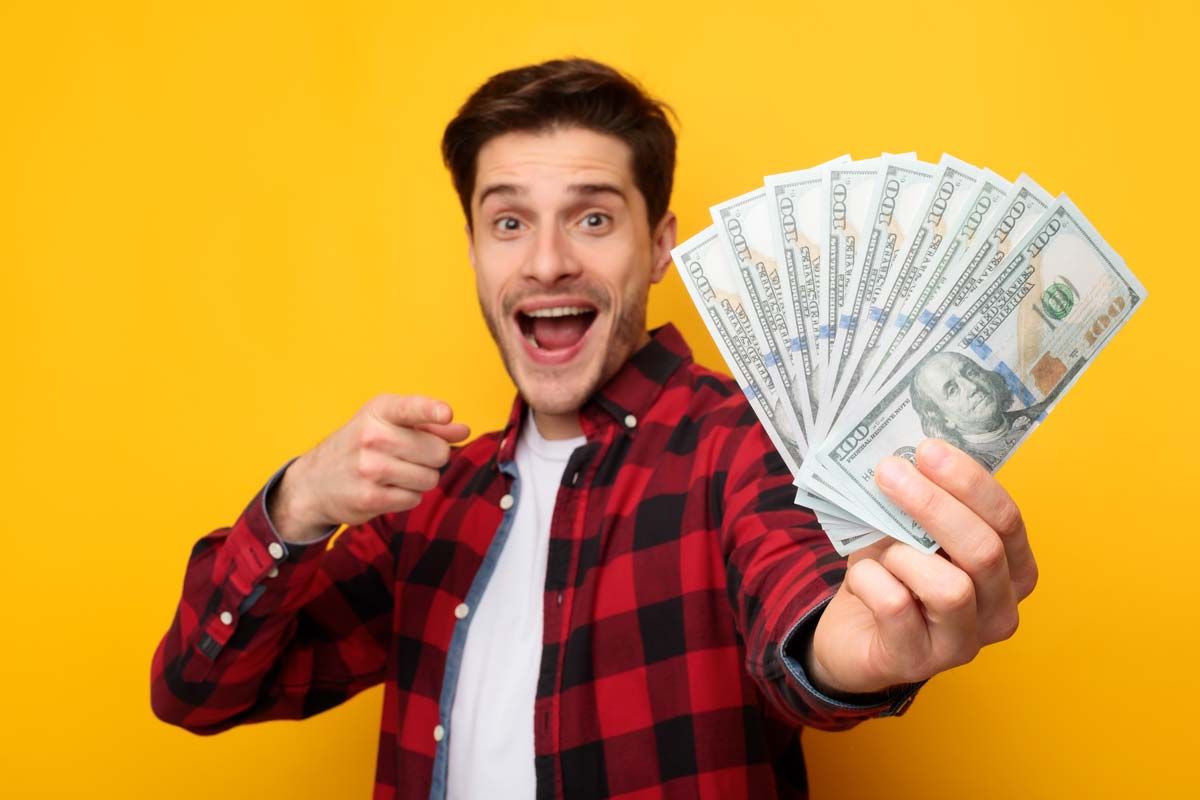 An excited man holding U.S. cash, representing recent settlement checks in the mail.