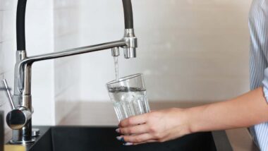 Close up of a woman filling a glass with water from a faucet, representing the drinking water contamination class action.