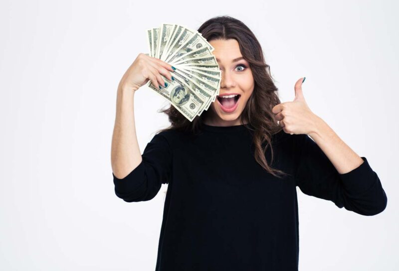 An excited woman holding cash and giving a thumbs up, representing checks in the mail in April.
