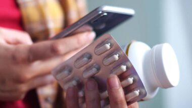 Close up of a woman holding pills and using her smartphone to order medicine, representing the Done Global Adderall arrests.