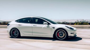 Side view of a white Tesla Model Y driving down a hgihway, representing the Tesla recall.