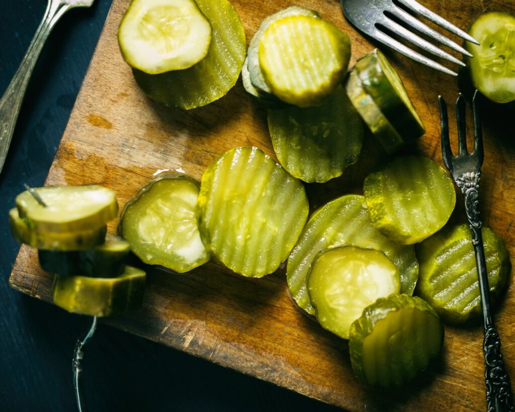 Top view of several pickle slices on a cutting board with antique forks.