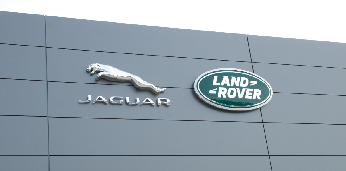 Jaguar Land Rover dealership with green oval logo on front of building with sky background.