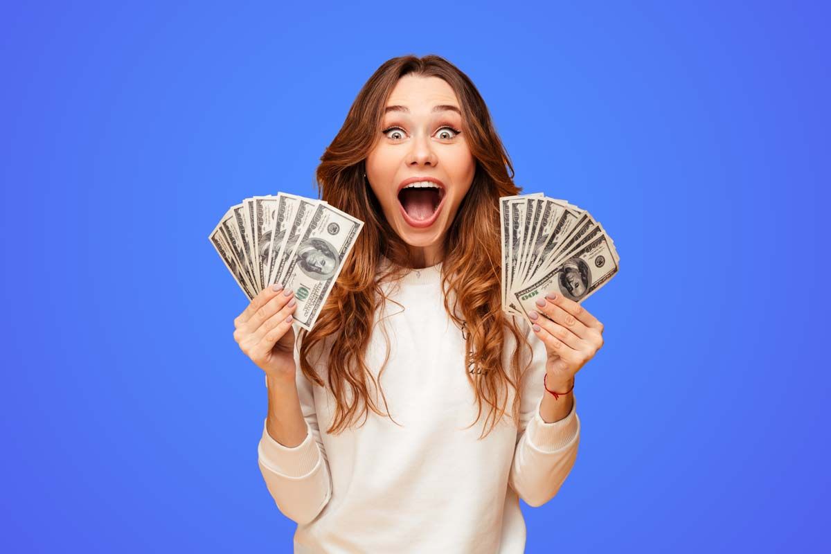 An excited woman holding U.S. cash, representing checks in the mail.