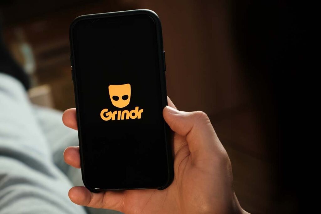 Close up of a man holding a smartphone with the Grindr logo displayed, representing the Grindr lawsuit.