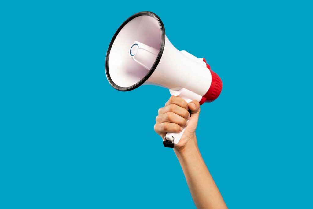 Close up of a hand holding a megaphone against a blue background.