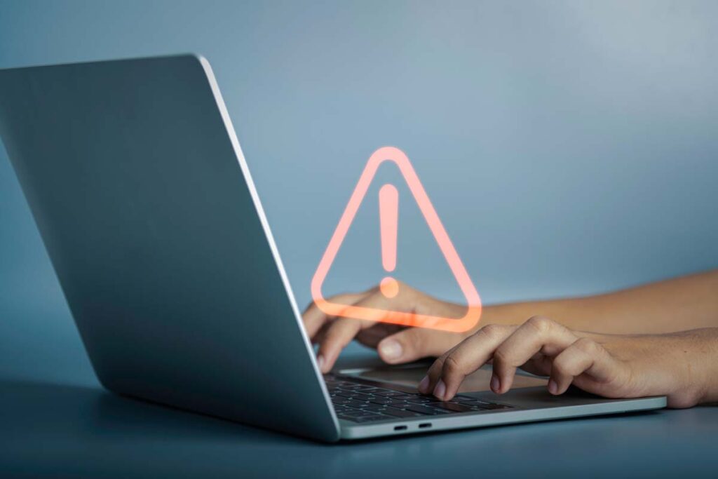 Close up of a woman typing on a laptop with a warning symbol overlay, representing recent data breach lawsuits and settlements.