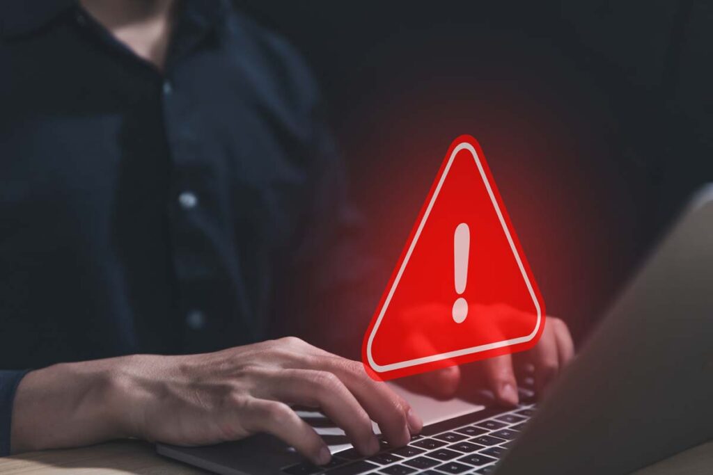 Close up of hands typing on a keyboard with a warning symbol overlay, representing the RockYou2024 data breach.