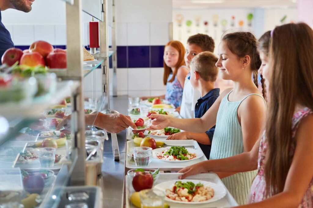 School children in line for food at the school cafeteria, representing school lunch payment junk fees.