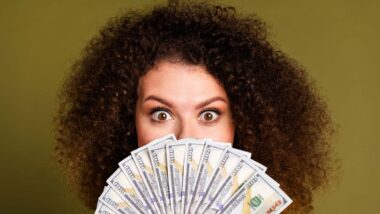 Close up of a surprised woman holding U.S. cash, representing checks in the mail.