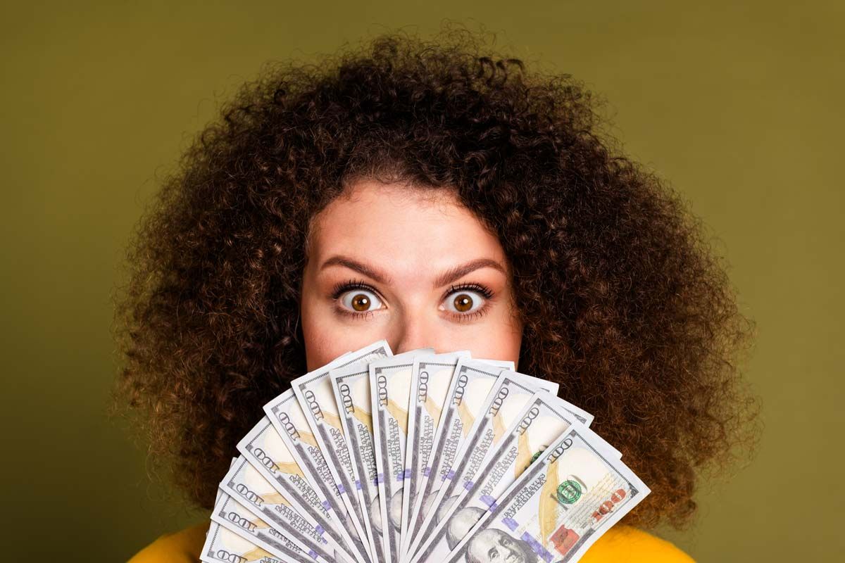 Close up of a surprised woman holding U.S. cash, representing checks in the mail.
