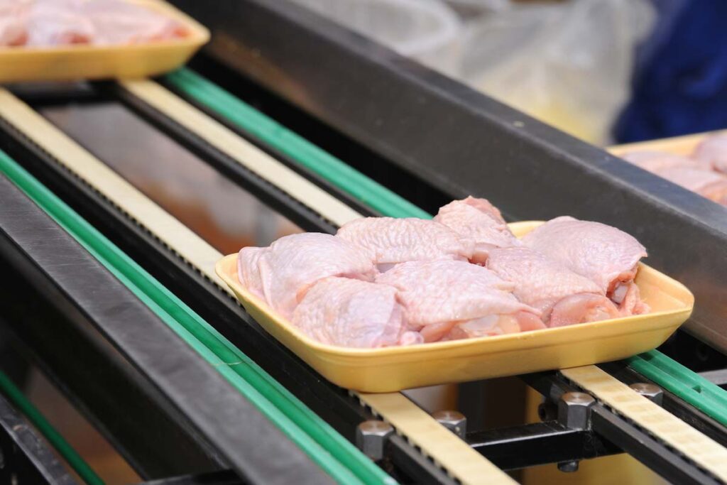 Close up of raw chicken in a manufacturing facility, representing OK Foods chicken price-fixing settlement.