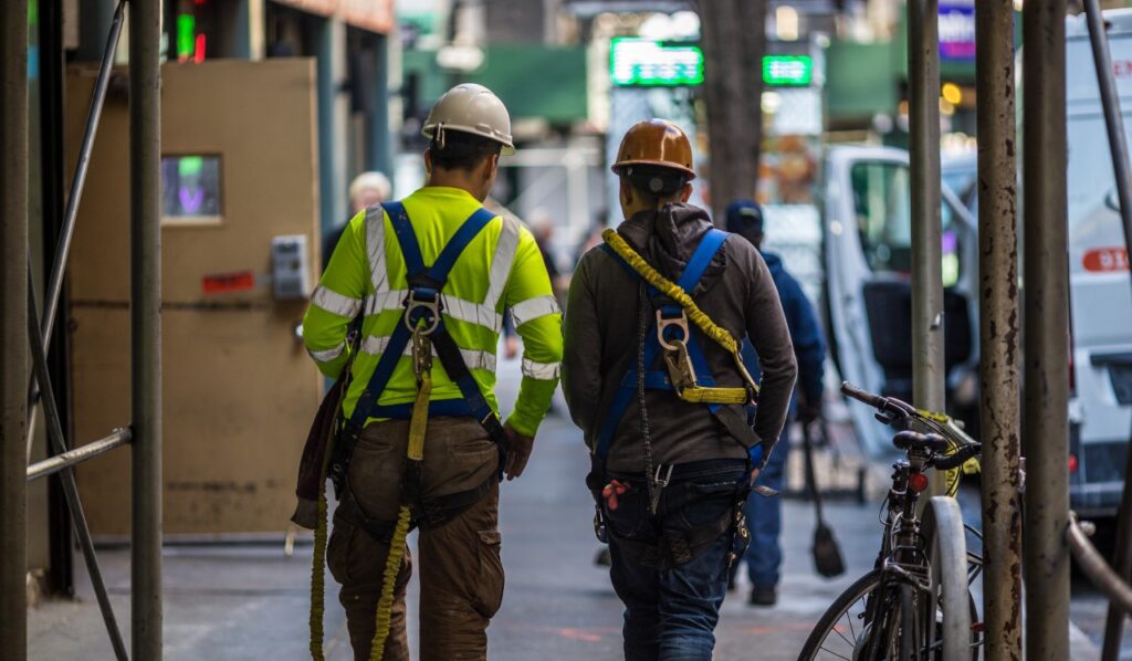 Two construction workers walk together down a New York City sidewalk