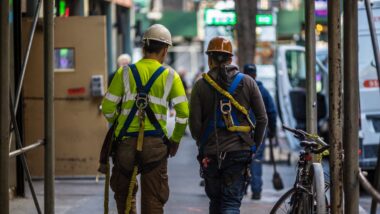 Two construction workers walk together down a New York City sidewalk
