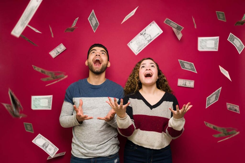 Young excited man and woman throwing cash into the air, representing recent class action rebates.