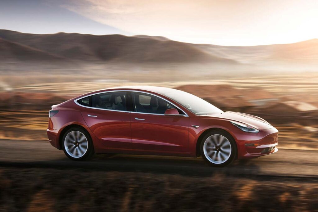 A red Tesla model 3 driving along a roadway, representing the Tesla recall.