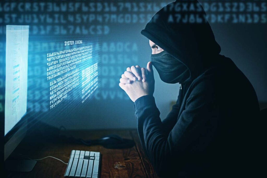 Side view of a hooded hacker using a computer, representing the National Public Data data breach.