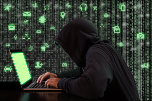 Hacker in a black hoodie working on a laptop, with green digital data images in the background