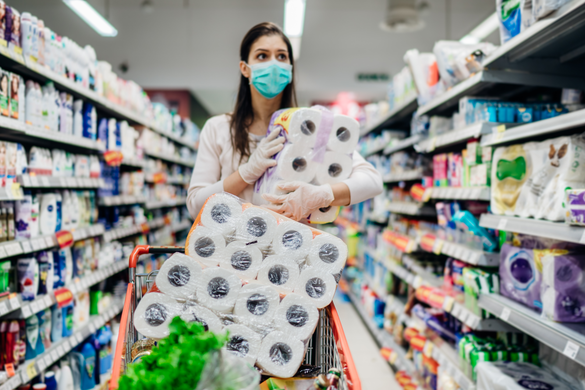 Woman shopping in a store for toilet paper while wearing a medical face mask and gloves