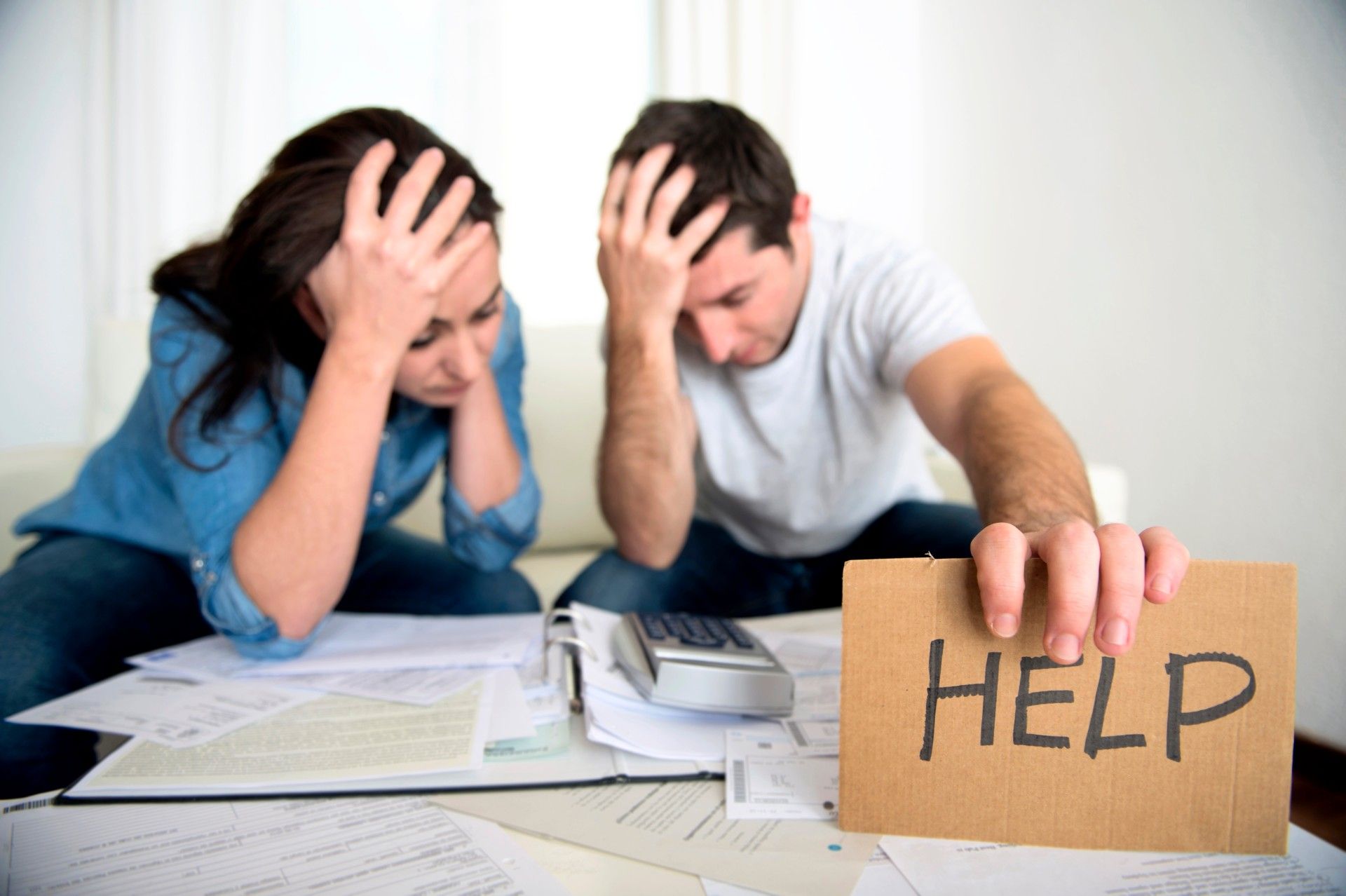 Couple stressed out over bills; man holds sign that says "help"