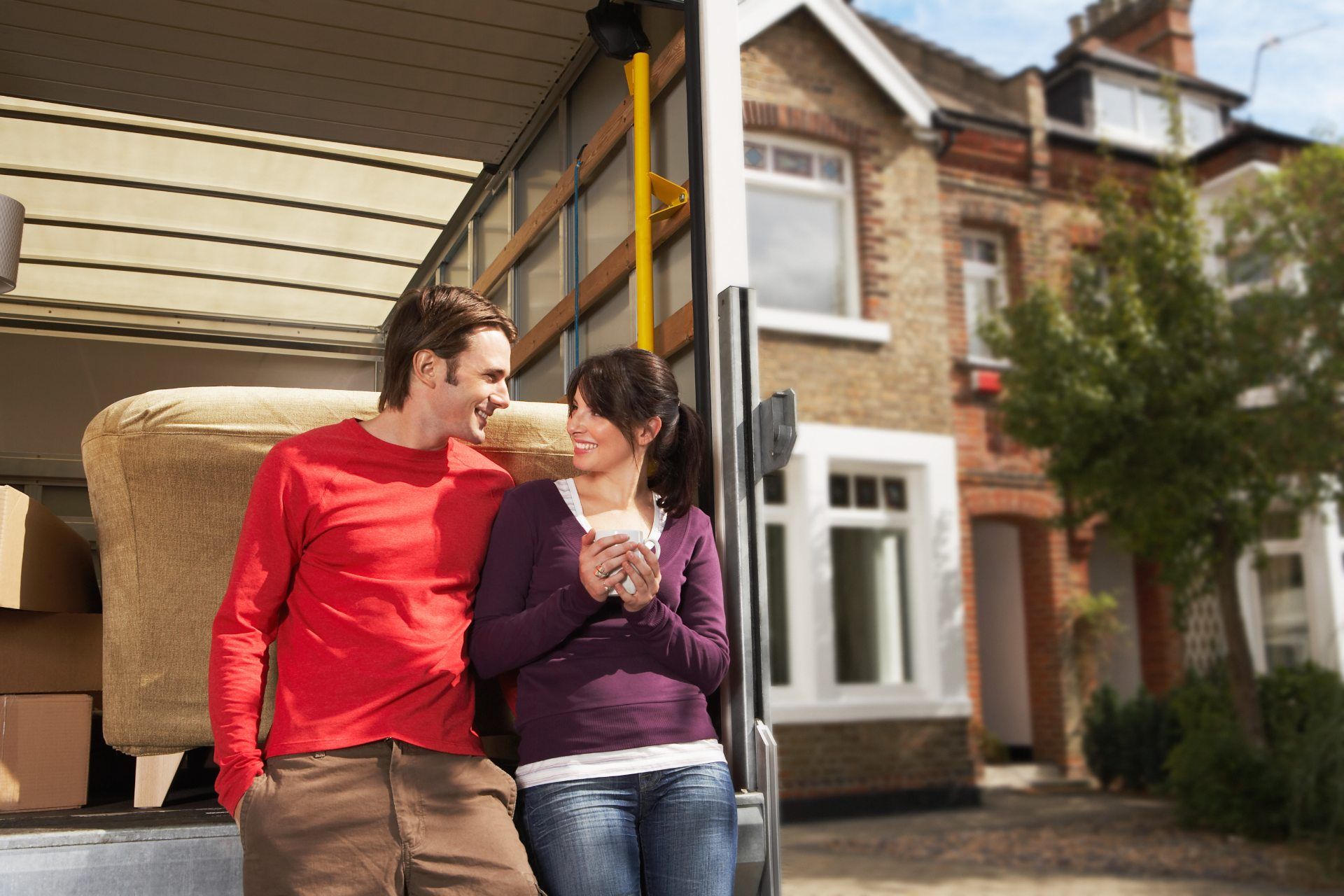 Couple leaning on back of open moving van with house in the background