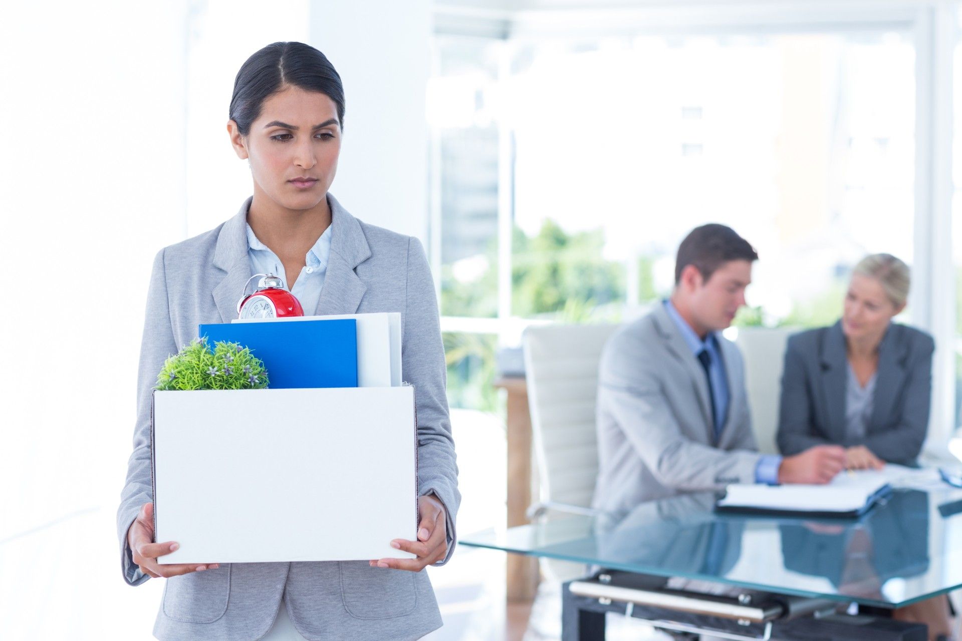 Woman carries box of desk contents after being fired from office - redundancy pay