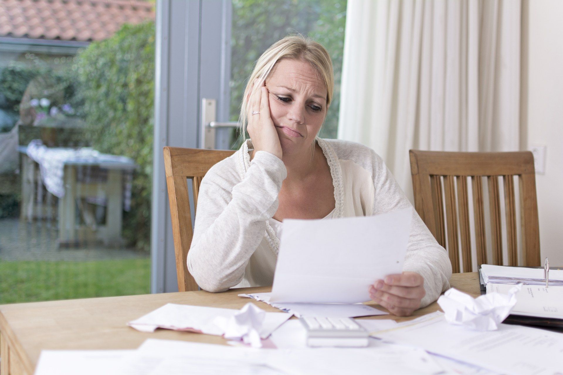 Woman holds paper at kitchen table with papers strewn around - mortgage holiday