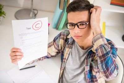 Teen boy in glasses holds a test with a "C" grade circled in red - A-level exam grades