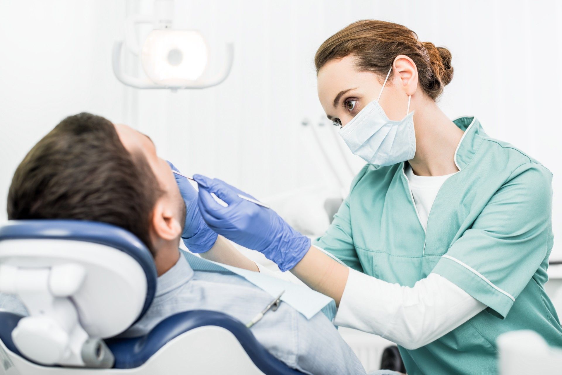 Female dentist in mask and green scrubs works on male patient's teeth - bda breach