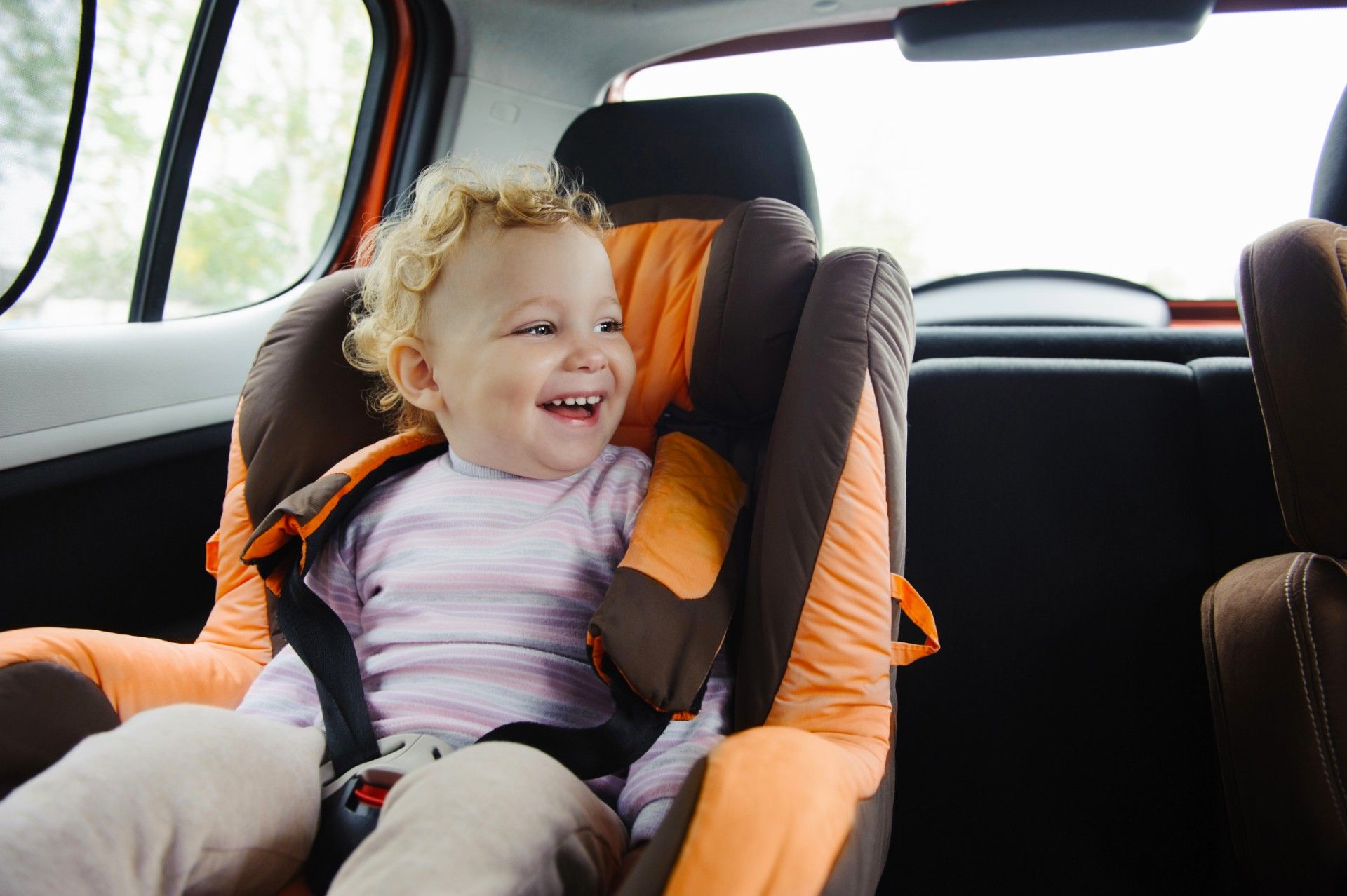 Child with curly hair sits in car seat - rented car seats