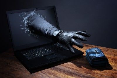 Arm with black glove reaches through laptop screen for wallet lying on table - scam victims